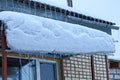 A series of icicles on the roof of the porch under the snow by the brick wall with a window Royalty Free Stock Photo