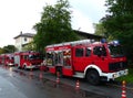 Series of red fire trucks parked in a line on a street, separated by traffic cones.