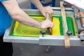 Serigraphy silk screen print process at clothes factory. Frame, squeegee and plastisol color paints