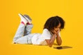 Serious adolescent african american girl in white t-shirt lies on floor, watching online lesson video