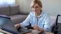 Serious adult lady in wheelchair entering card number on laptop, shopping online