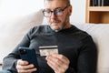 Serious adult unshaven man using cellphone and credit card