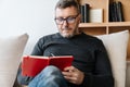 Serious adult unshaven man writing down notes while sitting on couch