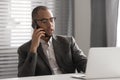 Serious African American businessman talking on phone, using laptop