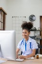 Serious African American doctor working in her office at clinic in white medical gown and stethoscope busy working on computer Royalty Free Stock Photo