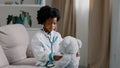 Serious african american kid girl sitting in room on couch in medical uniform pretending to be doctor little child Royalty Free Stock Photo
