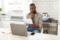 Serious african american man sitting in kitchen working looking at paperwork and using laptop Royalty Free Stock Photo