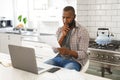 Serious african american man sitting in kitchen working looking at paperwork and using laptop Royalty Free Stock Photo