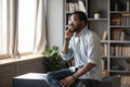 Serious African American man talking on phone, sitting on desk