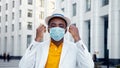 Serious African American man in yellow t shirt under white jacket and facial mask looks straight Royalty Free Stock Photo