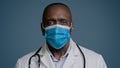 Serious african american mature man doctor surgeon therapist in medical gown and protective mask looking at camera Royalty Free Stock Photo