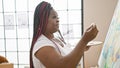 Serious african american woman artist beautifully drawing a portrait, concentrating on her canvas in a cozy indoor art studio,