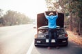 Serious african man looking his old broken car with raised hood on the highway road Royalty Free Stock Photo