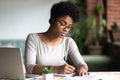 Serious african woman studying using internet holding pen writing notes