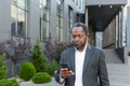 Serious afro american boss in business suit walking outside office building, mature man holding phone, businessman Royalty Free Stock Photo