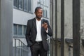 Serious afro american boss in business suit walking outside office building, mature man holding phone, businessman Royalty Free Stock Photo