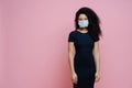 Serious Afro American woman wears disposable medical mask on face, being on self isolation during quarantine, stays at home alone