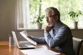 Serious aged businessman read documents at desk in home office