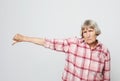 Serious aged woman pointing finger down. Portrait of expressive grandmother with pink shirt.