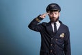 Serious airplane pilot in professional uniform saluting