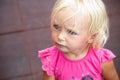 Serious angry baby girl looking left. Blond blu eye kid in pink t-shirt portrait. Blurred protective rubber pavement Royalty Free Stock Photo