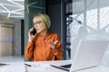 Serious and angry female boss talking on the phone at workplace, business woman working with laptop Royalty Free Stock Photo