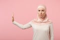 Serious arabian muslim woman in hijab light clothes posing isolated on pink background in studio. People religious Islam