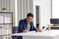 Asia businessman making notes, working with paper documents, writing report at workplace, focused employee doing economic