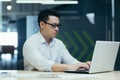 Serious asian boss in glasses working and typing on laptop, man concentrated in modern office. Royalty Free Stock Photo