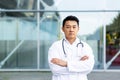 Serious asian doctor with folded arms on background of modern clinic outdoors Royalty Free Stock Photo