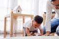 Serious Asian little boy crawling on floor while young father sitting next to him in living room Royalty Free Stock Photo