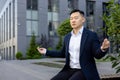 Serious Asian male businessman sitting on bench near working office in lotus position and meditating with closed eyes Royalty Free Stock Photo