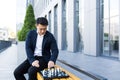 Serious asian man playing chess outside, businessman thinking playing chess sitting on bench near office center Royalty Free Stock Photo