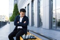 Serious asian man playing chess outside, businessman thinking playing chess sitting on bench near office center Royalty Free Stock Photo