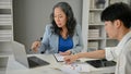 A serious Asian senior businesswoman focuses on working with a young male worker Royalty Free Stock Photo