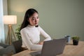 A serious Asian woman focuses on her work on laptop at a table in her living room Royalty Free Stock Photo