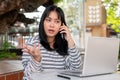 A serious Asian woman is talking on the phone with someone while working remotely at a cafe Royalty Free Stock Photo