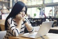 Serious asian woman thinking of problem to working a difficult assignment in a desktop, using laptop computer sitting alone at