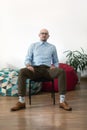 Serious bald business man in glasses sitting on office chair in room with poufs and plant and looking at camera. Royalty Free Stock Photo