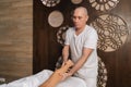 Serious bald male masseur massaging lower part of leg to young unrecognizable woman in spa salon. Professional therapist Royalty Free Stock Photo