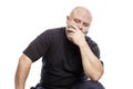 A serious bald middle-aged man in a black T-shirt is sitting with his hand in his face. Isolated over white background Royalty Free Stock Photo