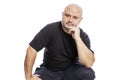 A serious bald middle-aged man in a black T-shirt is sitting with his hand in his face. Isolated over white background Royalty Free Stock Photo