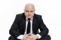 A serious, bald, middle-aged man in a strict black suit sits and stares in front of him. Business success and complexity. White Royalty Free Stock Photo