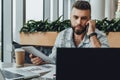 Serious bearded hipster man sits in office, talking on phone while holding tablet computer,looking at laptop screen. Royalty Free Stock Photo