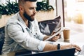 Serious bearded hipster man sitting in office at desk,working on laptop,holding tablet computer,looking at laptop screen Royalty Free Stock Photo