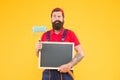 Serious bearded man painter worker in boiler suit uniform using paint roller tool for painting wall and hold chalkboard Royalty Free Stock Photo