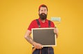 serious bearded man painter worker in boiler suit uniform using paint roller tool for painting wall and hold chalkboard Royalty Free Stock Photo