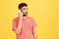 Serious bearded man in red striped t-shirt holding phone near his ear, talking with friends, favorable tariff for calls in roaming Royalty Free Stock Photo