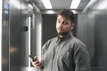 Serious bearded man in a shirt stands in the elevator with a smartphone in his hand and is concentrated in the camera. Portrait of Royalty Free Stock Photo