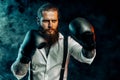 Serious bearded man in white shirt wears boxing gloves and ready to fight in smoke. Man self defense